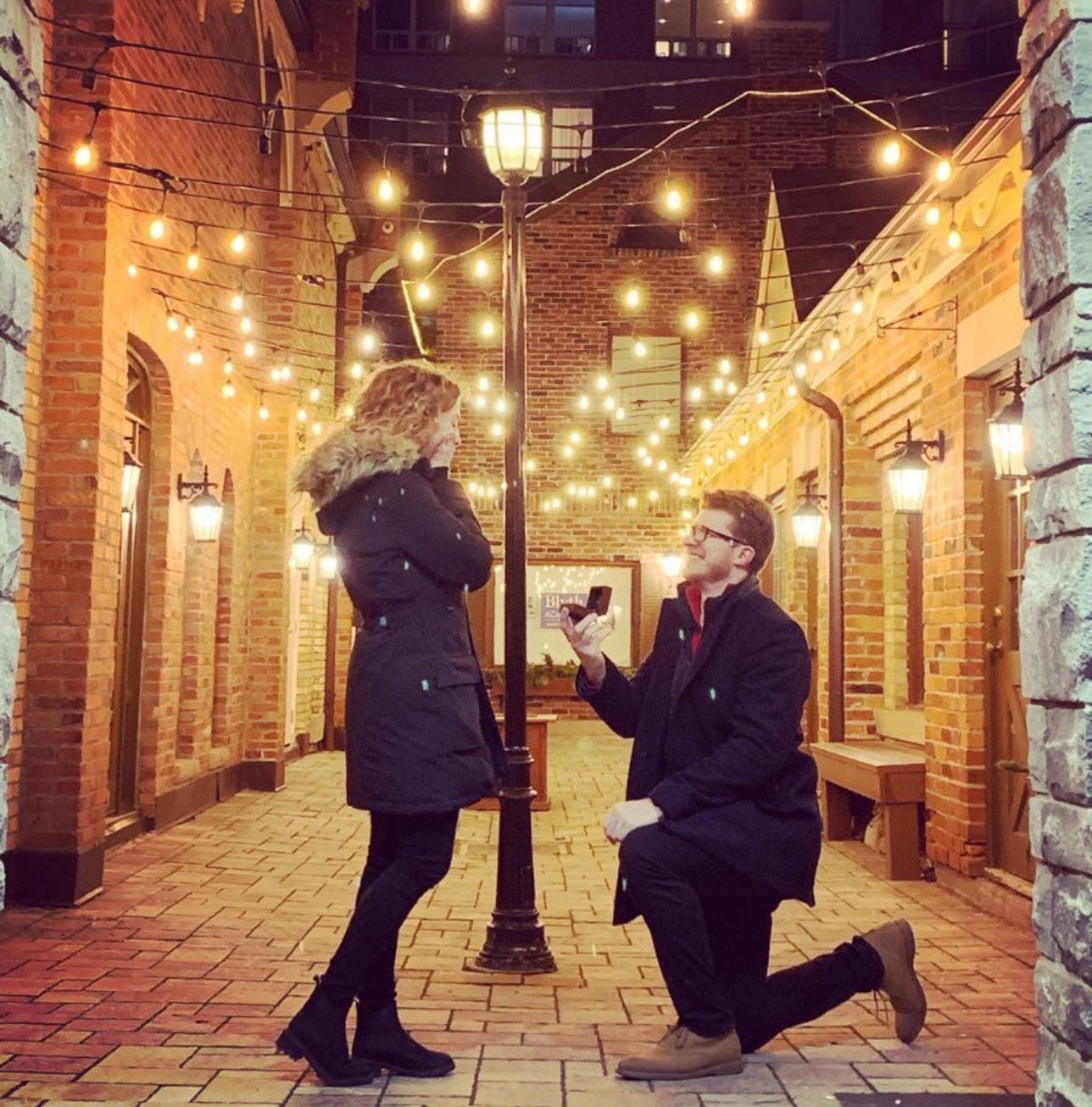 Night-time proposal under string lights in Toronto's Distillery District