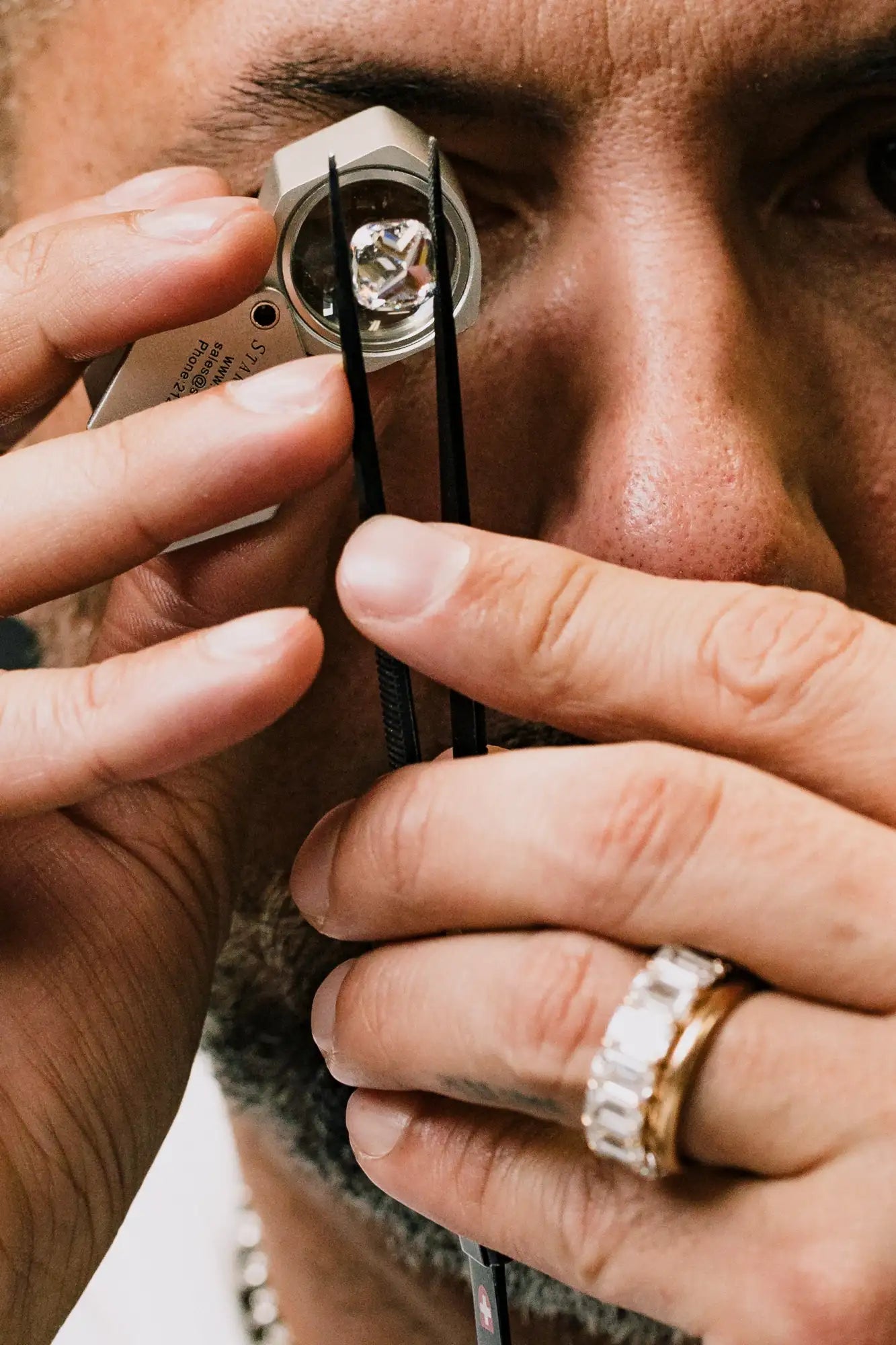 A clear, faceted diamond held securely in a jeweler’s magnifying loupe with black tweezers.