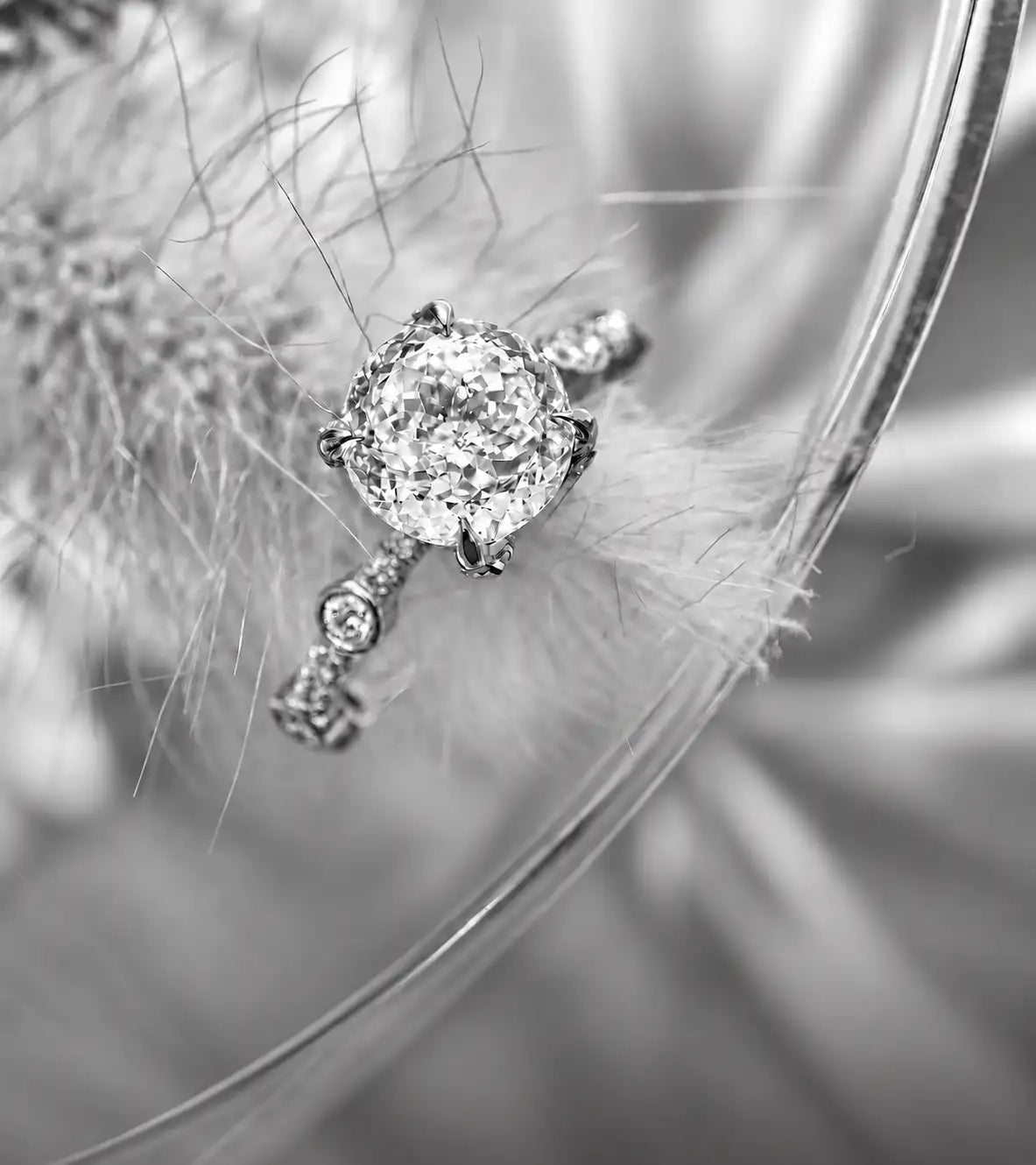 A sparkling diamond engagement ring with a central round-cut stone set in a sleek, metallic band adorned with smaller diamonds along its side.
