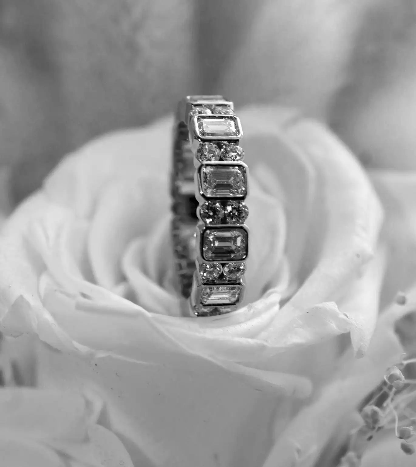 An elegant diamond eternity band featuring rectangular and round-cut stones set in a sleek, polished metal.