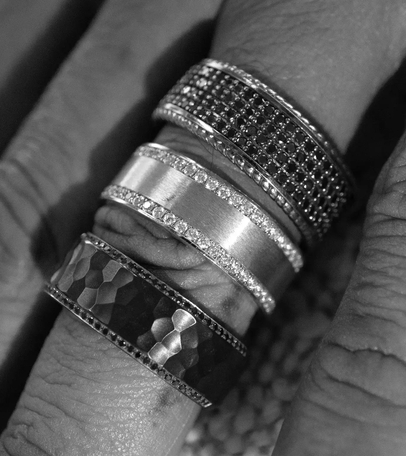 Three stacked rings on a finger, featuring different designs including pave-set stones and hammered metal textures.